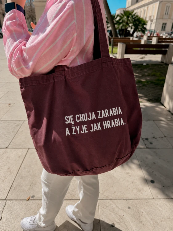 Burgundowa torba na miejskim chodniku.png